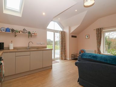 A kitchen and living space with cabinets a sink sofa and windows at Y Felin in Caernarfon