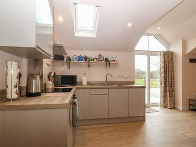 A kitchen with cabinets a countertop a microwave a kettle and a door leading outside at Y Felin in Caernarfon