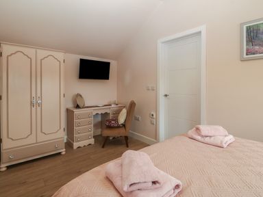 A bedroom with a bed folded towels a wardrobe a dressing table a chair and a wall-mounted television at Y Felin in Caernarfon