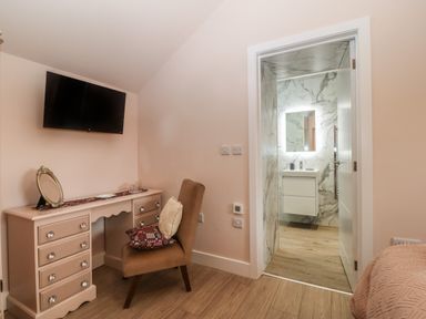 A bedroom with a wall mounted TV a vanity desk and chair and an open door to a bathroom with a lit mirror at Y Felin in Caernarfon