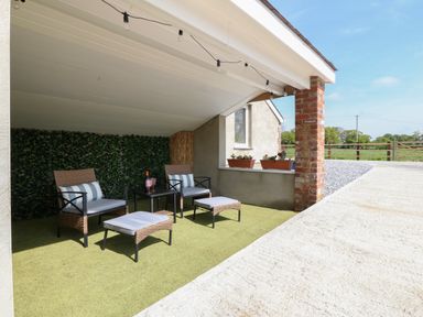 A covered outdoor seating area with two chairs and two footstools with cushions and a side table at Y Felin in Caernarfon