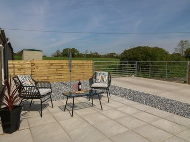 An outdoor patio with two chairs and a glass table with a bottle and glasses at Y Felin in Caernarfon