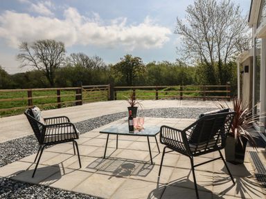 An outdoor patio with two black chairs and a glass table with a bottle and glasses at Y Felin in Caernarfon