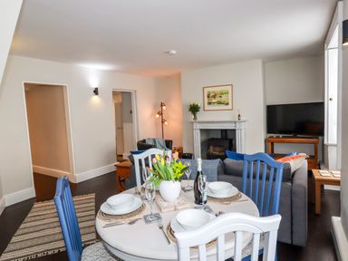 A dining table set with plates and glasses and a vase of flowers in a living room with sofas a fireplace and a television at Carew House Cottage in St Day