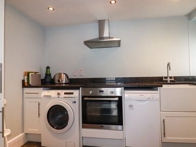 A kitchen with a washing machine oven dishwasher sink toaster chopping boards and extractor fan at Carew House Cottage in St Day