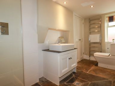 A bathroom with a sink cabinet a toilet a heated towel rail and a window at Carew House Cottage in St Day