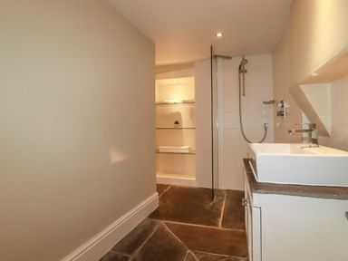 A bathroom with a sink countertop shower area and shelves with towels and a plant at Carew House Cottage St Day