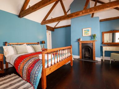 A bedroom with a wooden bed a colorful bedspread and a fireplace at Carew House Cottage in St Day