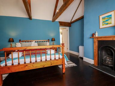A bedroom with a wooden bed frame blue walls a fireplace and ceiling beams at Carew House Cottage in St Day