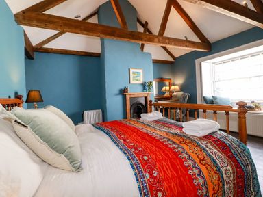 A bedroom with wooden beams a bed with colorful bedding and two folded towels at Carew House Cottage in St Day