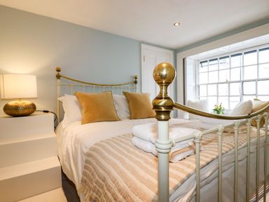 A bedroom with a metal bed frame pillows lamps and a window seat at Carew House Cottage in St Day