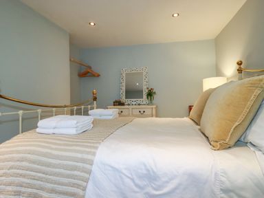 A bedroom with a bed, pillows, folded towels, a dresser with a mirror, a lamp, and a hanging rod with hangers at Carew House Cottage in St Day