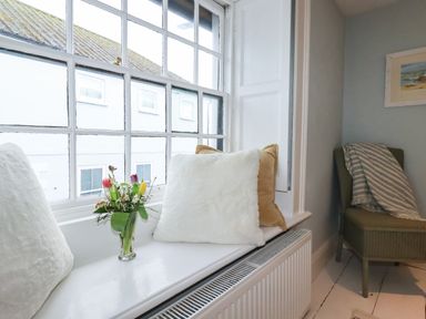 A window seat with cushions and a vase of flowers beside a chair with a striped blanket at Carew House Cottage in St Day