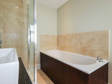 A bathroom with a bathtub with tiled walls and a glass shower enclosure at Carew House Cottage in St Day