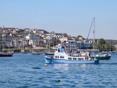 A boat with people on a body of water near a town with houses and other boats in the background at Carew House Cottage in St Day