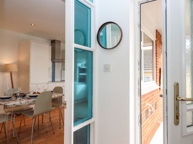 A dining area with table and chairs next to a kitchen and an open door to an outside brick wall at Sandy Toes in Paignton