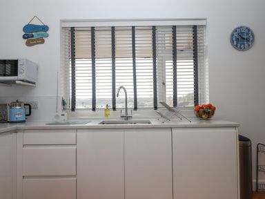 A kitchen with a sink dish rack fruit bowl microwave and clock at Sandy Toes in Paignton