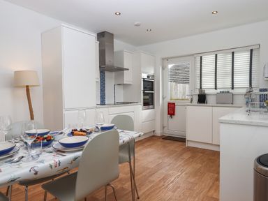 A kitchen with a dining table set with plates and glasses next to white cabinets and a door with a window at Sandy Toes in Paignton