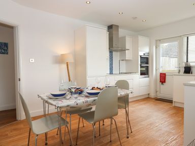 A kitchen with a small dining table set for four and modern white cabinets at Sandy Toes in Paignton