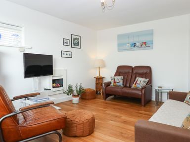 A living room with brown leather seats a wall mounted television and wooden flooring at Sandy Toes in Paignton