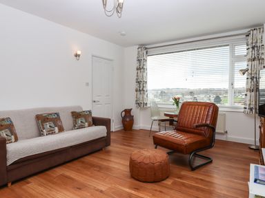 A living room with brown sofa and cushions a leather chair and ottoman and window with blinds at Sandy Toes in Paignton