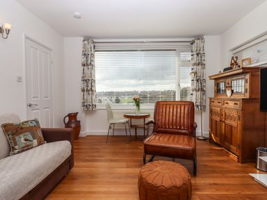 A living room with a brown leather chair and wooden cabinet near a window with blinds at Sandy Toes Paignton