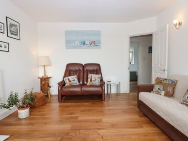 A living room with a brown leather loveseat, a sofa with patterned cushions, a wooden side table with a lamp, and a potted plant at Sandy Toes in Paignton