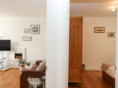 A living room with a brown leather sofa and a television next to a bedroom with a wooden wardrobe and a bed at Sandy Toes Paignton