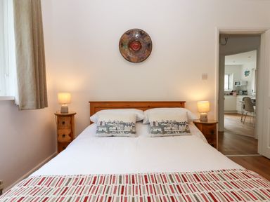 A bedroom with a double bed two bedside tables with lamps and a view into a kitchen at Sandy Toes in Paignton