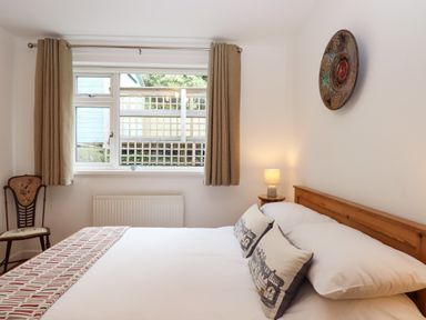 A bedroom with a bed two decorative pillows a wooden chair a window with curtains and a small lamp on a bedside table at Sandy Toes in Paignton