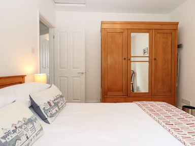 A bedroom with a bed with pillows a wooden wardrobe with a mirror a lamp and an open door at Sandy Toes in Paignton