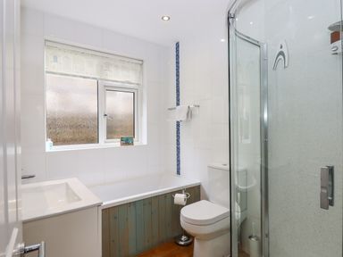 A bathroom with a bathtub, toilet, shower enclosure, sink, and frosted window at Sandy Toes in Paignton