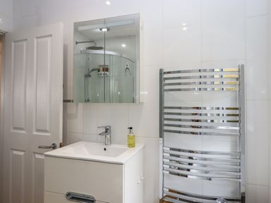 A bathroom with a white sink cabinet a mirror cabinet a glass shower enclosure and a chrome towel radiator at Sandy Toes in Paignton