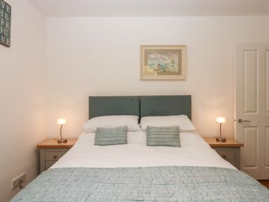 A bedroom with a double bed two bedside tables with lamps and a framed painting above the bed at Sandy Toes in Paignton