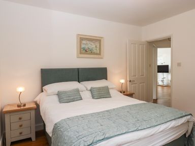 A bedroom with a double bed two bedside tables with lamps and a painting above the bed at Sandy Toes in Paignton