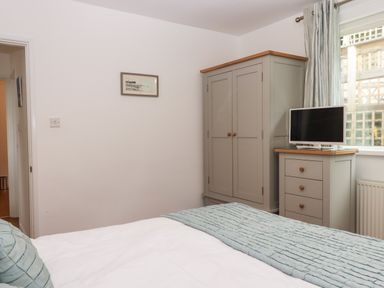 A bedroom with a wardrobe a chest of drawers with a TV and a bed with pillows and a blanket at Sandy Toes in Paignton