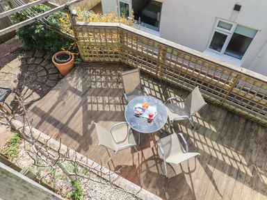 A patio with a round glass table and four chairs with snacks and drinks on the table at Sandy Toes in Paignton