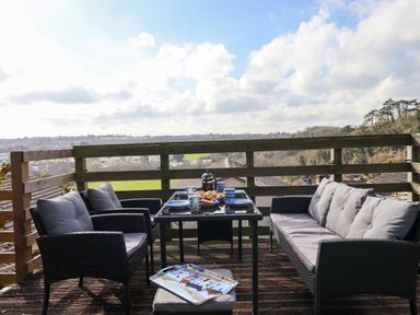 An outdoor wooden deck with cushioned chairs and a table set with blue plates and cups at Sandy Toes in Paignton