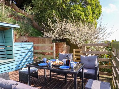 An outdoor patio with a glass table set for tea with blue plates and striped mugs at Sandy Toes in Paignton
