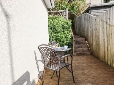 An outdoor wooden deck with a metal table and chairs and stairs leading up next to a wooden fence at Sandy Toes in Paignton