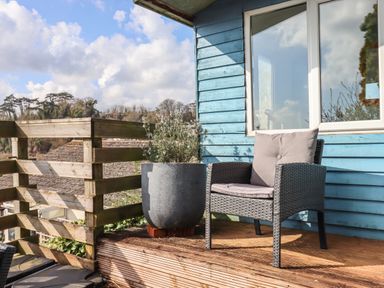 A patio chair with cushions next to a planter on a wooden deck outside a blue house at Sandy Toes in Paignton