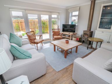 A living room with sofas chairs a coffee table a television and a fireplace at Turnstone in Beadnell