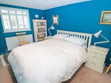 A bedroom with a white bed white bedside tables a bookshelf a wooden chair and blue walls at Turnstone in Beadnell
