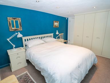 A bedroom with a double bed white bedding blue painted wall wardrobes bedside tables with lamps and a chair at Turnstone Beadnell