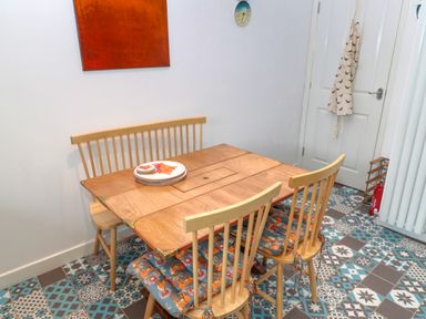 A dining area with a wooden table and chairs with patterned cushions on a tiled floor at Turnstone in Beadnell