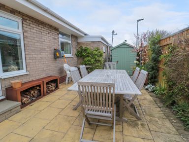 An outdoor patio area with a wooden dining table and chairs a small green shed and plants along the fence at Turnstone Beadnell