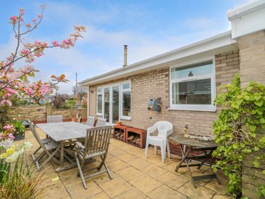 An outdoor patio with wooden table and chairs white plastic chair and small round table at Turnstone in Beadnell