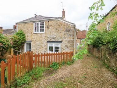 Stone house with white framed windows next to wooden fence and gravel path at Half Pint Cottage in Beaminster