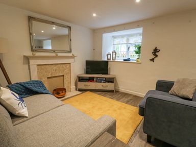 A living room with two sofas a television on a stand a fireplace with a mirror above and a window with plants at Half Pint Cottage in Beaminster
