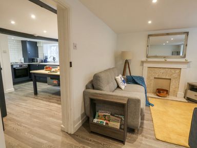 A living room with a gray sofa a blue blanket a floor lamp and a fireplace next to a kitchen with dark cabinets and a wooden island at Half Pint Cottage in Beaminster